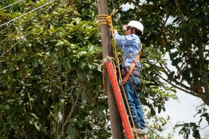 Male electrician wearing clothing, helmet and safety harness climbing on a light pole.