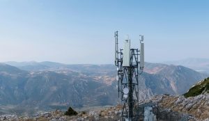 Cell tower. Mobile phone antenna aerial view. Rocky mountain and blue sky