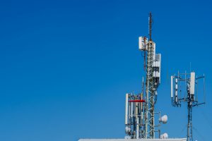 Close-up of tower with 6G, 5G, 4G cellular network antenna on blue sky background.