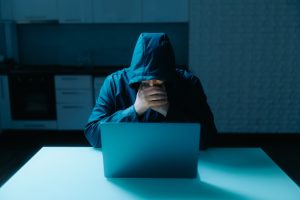 Modern Cyber Threat Hooded Hacker Sitting at Kitchen Table at Home